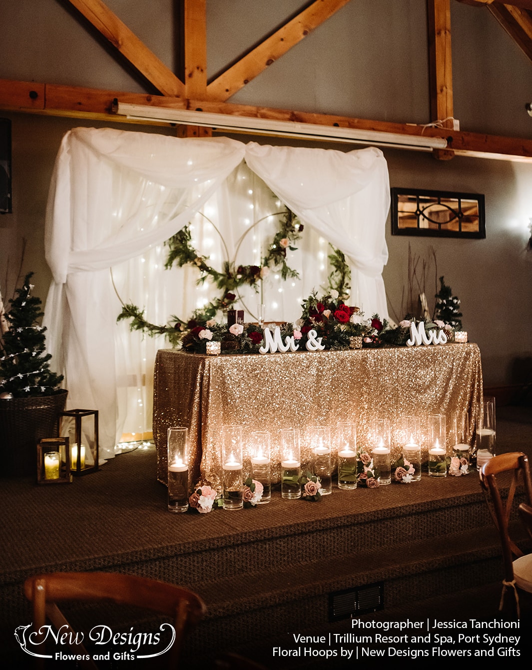 A wintery backdrop in a chalet venue, the center featuring 3 gold rings wrapped with greenery and a mix of burgundy white and blush flowers designs by new designs flowers and gifts
